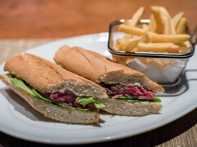 Sanduíche aus französischem Brot mit Rosbife und grünen Blättern, in der Mitte geschnitten, begleitet von Pommes in Metallkorb.