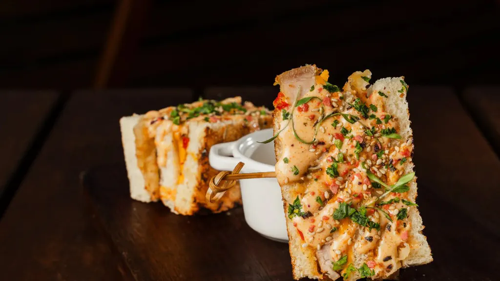 Sukulenter Schweinebauch, kombiniert mit Pfeffergelee, Ananas, Gurken und würzigen Aioli, in Brotform serviert