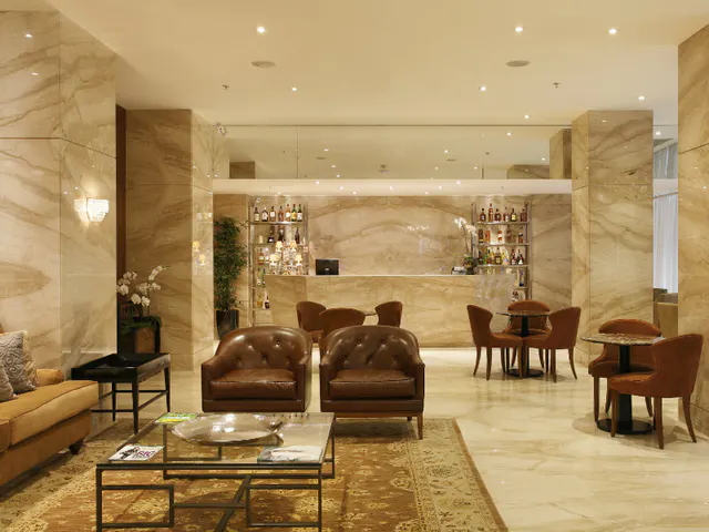 Hotel Lobby mit hellen Marmorwänden, braunen Ledersesseln, Tischen und bedruckten Teppichen