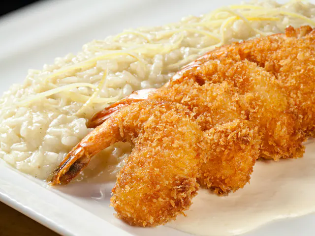 Prato com camarões empanados e crocantes servidos sobre risoto cremoso com queijo ralado