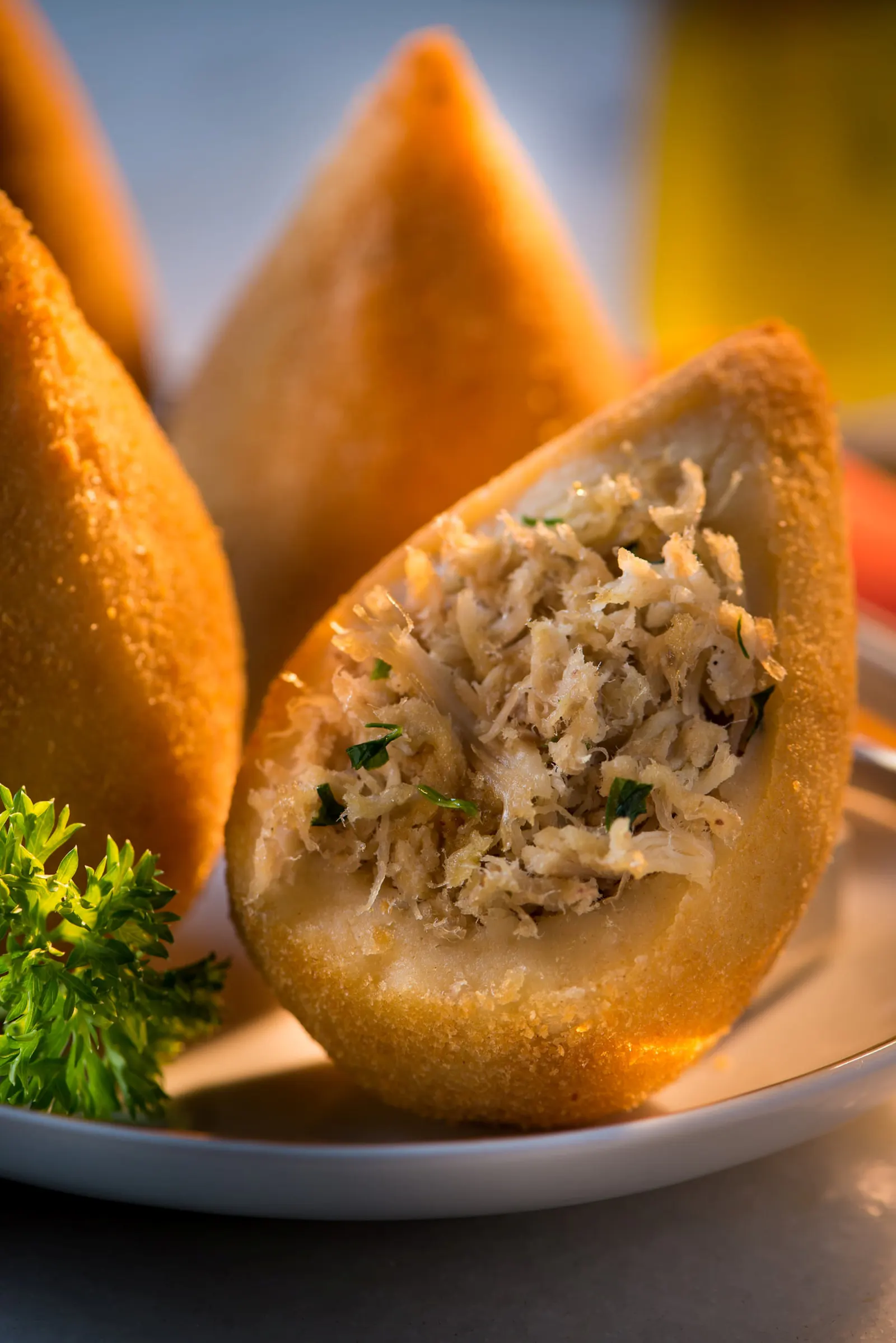 Coxinha abierta al medio mostrando el relleno de pollo desfiado con temperos, al lado de otras cojitas doradas